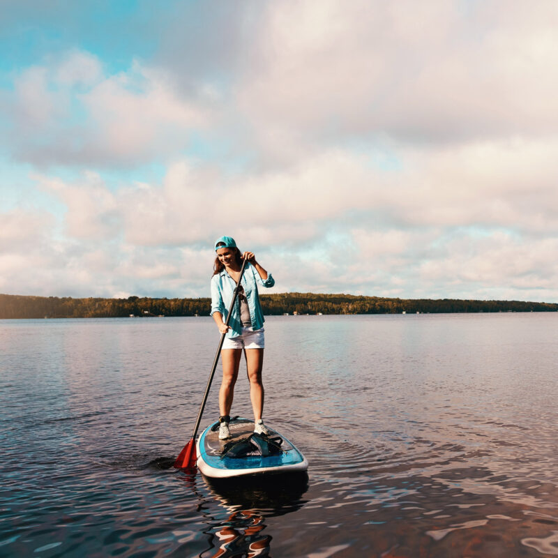 Woman, lake and smile for paddleboard on vacation with adventure
